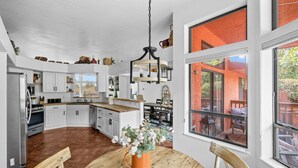 Een ruime keuken met witte kasten, een houten eettafel en een groot raam met uitzicht op de omgeving.