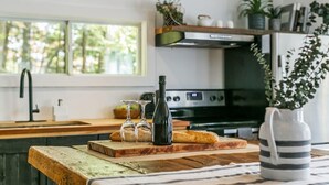 A kitchen with a wooden countertop, a cutting board, a bottle, two glasses, and a striped mug. - Spring Nature Retreat w/Hot Tub Near Owl’s Head (Mansonville)