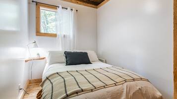 Un dormitorio con cama, mesita de noche, lámpara, ventana con cortinas y techo de madera.