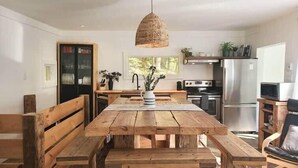 A modern kitchen with wooden benches, a hanging light fixture, and stainless steel appliances. - Spring Nature Retreat w/Hot Tub Near Owl’s Head (Mansonville)