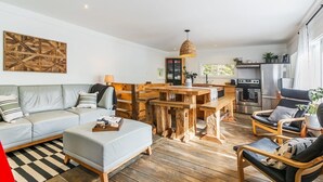 A modern living room with a sofa, ottoman, and wooden coffee table. There is a kitchen area with a refrigerator, oven, and dining table. - Spring Nature Retreat w/Hot Tub Near Owl’s Head (Mansonville)