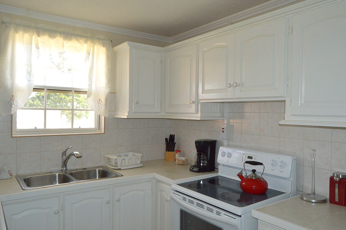 A kitchen with white cabinets, a double sink, a stove, and a window with curtains.