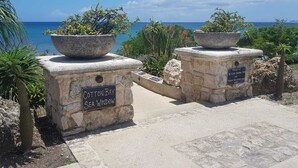 Uma trilha de pedra que leva a uma vista para o mar, com uma placa indicando 'Cotton Bay Sea Window'.