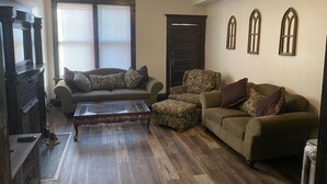 Un salon comprenant un canapé, un fauteuil, un pouf et une table basse.