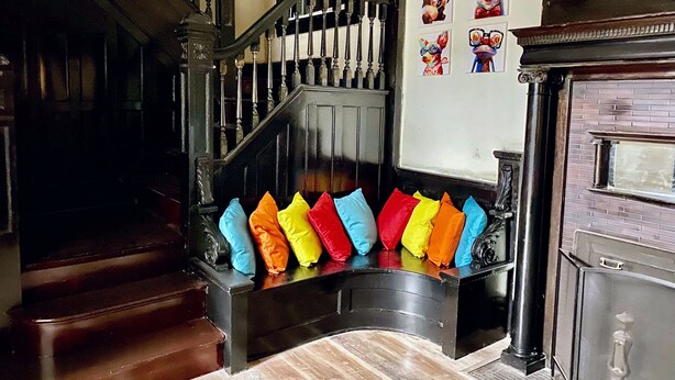Un escalier avec une rampe noire et un mur orné d’œuvres d’art colorées.