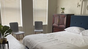 Une chambre à coucher comprenant un lit, deux chaises, une commode et un bureau agrémenté d’une plante.