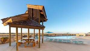 A wooden gazebo with a table and chairs, a pool with lounge chairs, and a clear sky. - Phoenix VII 004 Summer vacation dates available. Just steps to Pool and Beach!! (Orange Beach)