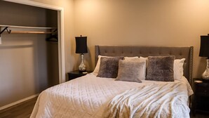 A bedroom with a large bed, two bedside tables with lamps, a closet with a hanging rod, and a ceiling light.