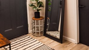 A hallway with a dark door, a large mirror, a potted plant, and a striped rug.