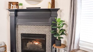 A fireplace with a hexagonal patterned surround, a mirror above it, and a potted plant to the right.