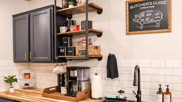 A modern kitchen with dark cabinets, a coffee station, and a butcher's guide on the wall.