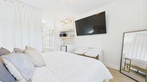 Ein Schlafzimmer mit einem großen Bett, einem an der Wand montierten Fernseher, einer weißen Kommode und einem Spiegel.