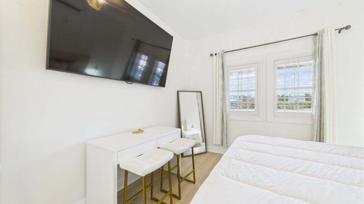 A hotel room with a bed, a desk with a mirror, and a TV mounted on the wall.