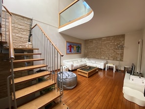 A modern living room with a wooden staircase, a white sofa set, a coffee table, and a stone wall. - Charming 1 bedroom House in Fabriano (Fabriano)