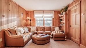 A cozy living room with a brown leather sectional sofa, a matching ottoman, and a wooden bookshelf.