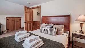 A neatly made bed with folded towels, a wooden headboard, and a bedside lamp.