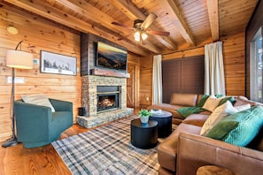 L’intérieur d’un chalet confortable, avec des murs en rondins de bois, une cheminée en pierre, des canapés en cuir et un tapis à carreaux.