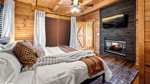 Een knus houten blokhut slaapkamer met een bed, een open haard en een plafondventilator.