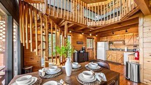 Een houten chalet van binnen, met een eethoek voor vier personen, een keuken en een trap naar een vide.