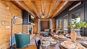 Een gezellig blokhutinterieur met een stenen openhaard, houten balkenplafond en een eethoek gedekt voor een maaltijd.