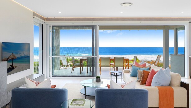 Un vaste espace de vie avec une grande porte vitrée donnant sur un balcon avec vue sur l’océan.