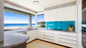 Une cuisine moderne avec vue sur la plage, des meubles blancs et un plan de travail bleu.