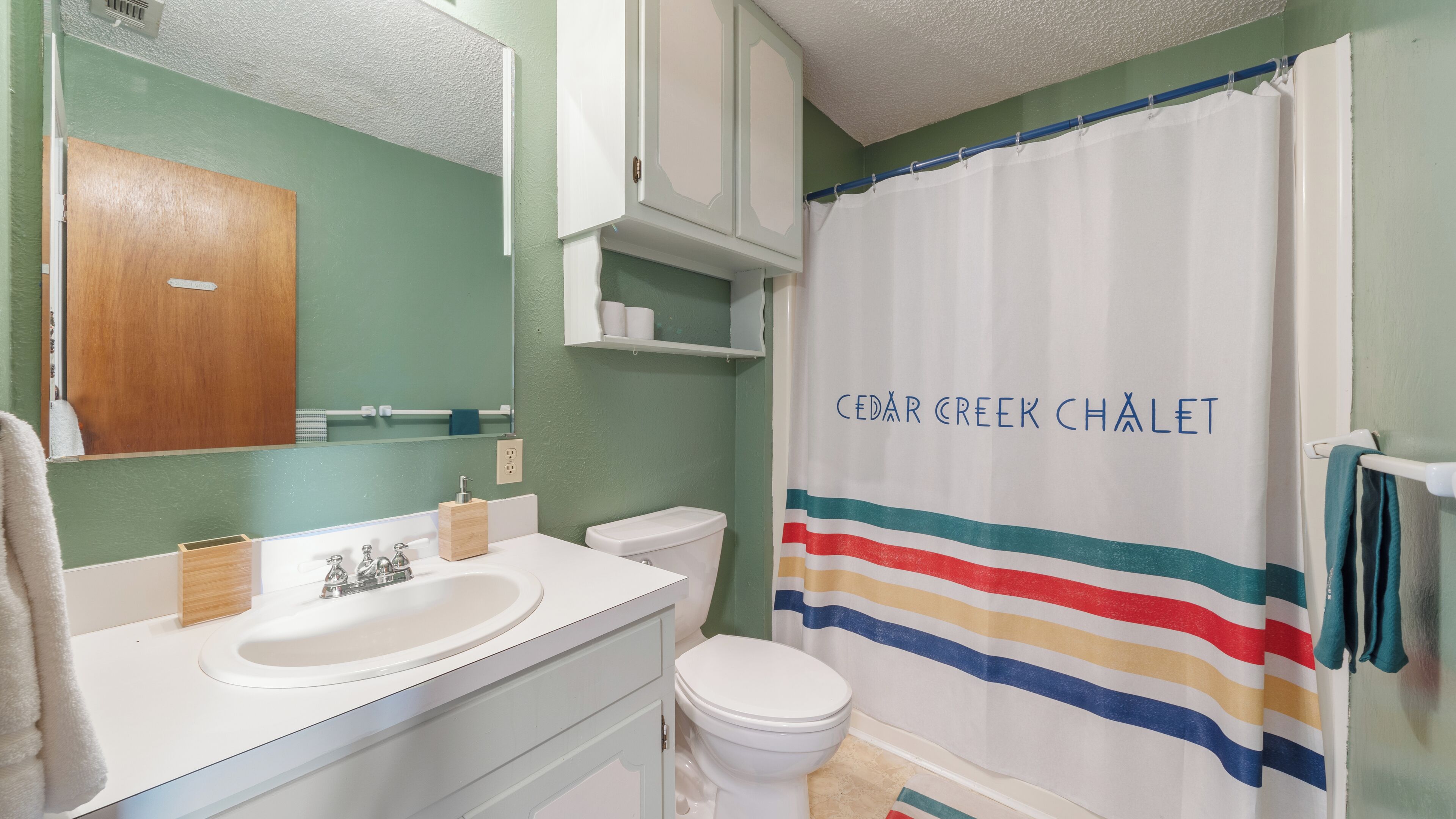 Een badkamer met een witte wastafel, een spiegel, een toilet en een douchegordijn met de tekst 'CEDAR CREEK CHALLET'.