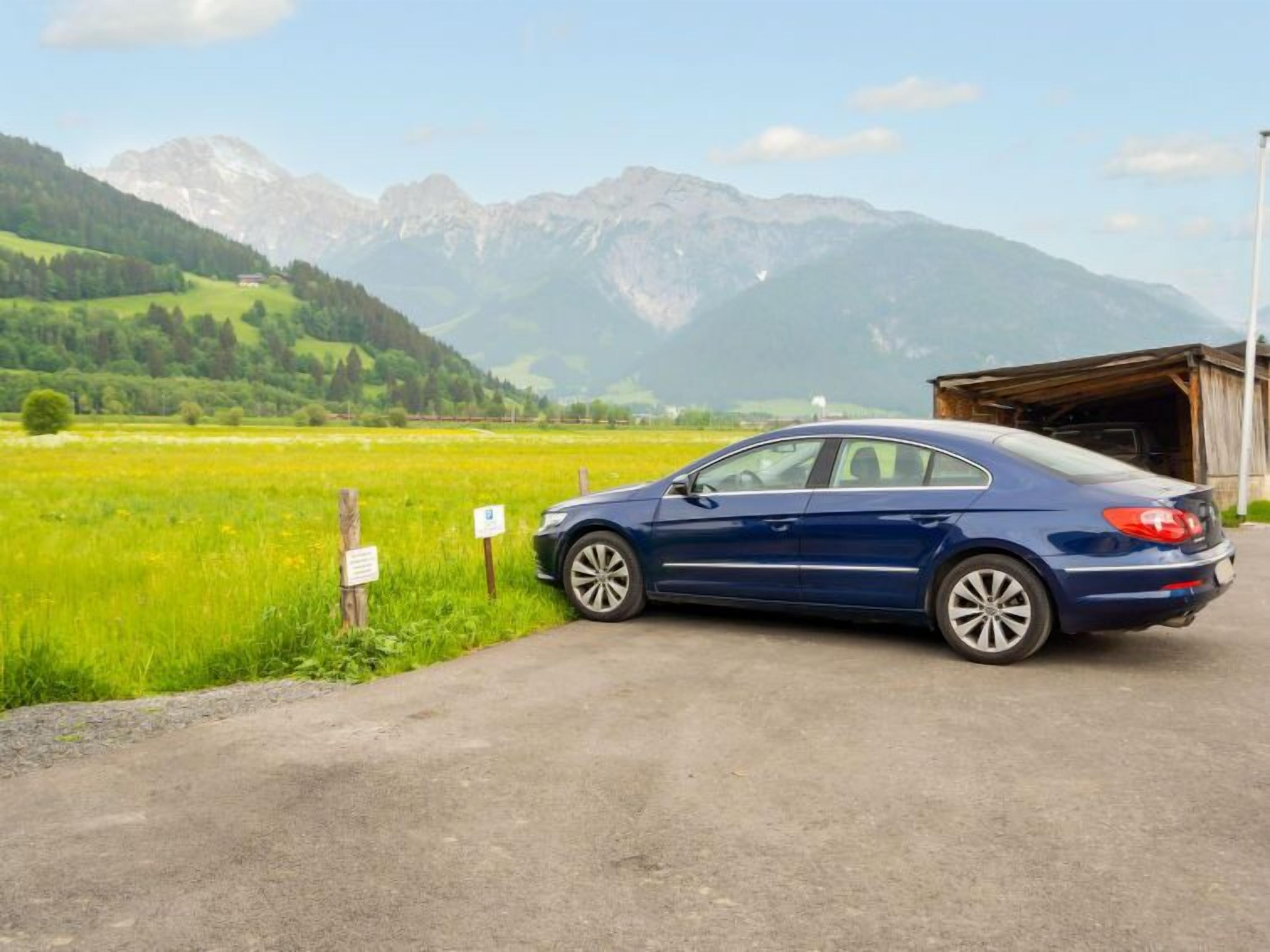 Ein blaues Auto auf einer Landstraße, mit Bergen im Hintergrund.
