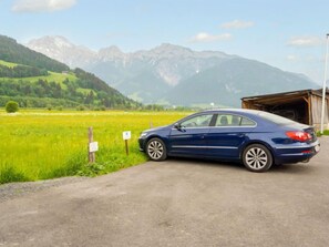 A blue car parked on a rural road with a mountain backdrop.