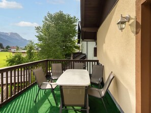 Un balcon avec une table et des chaises, une vue sur un champ verdoyant et des montagnes, et un bâtiment avec un mur de couleur beige et une lanterne.