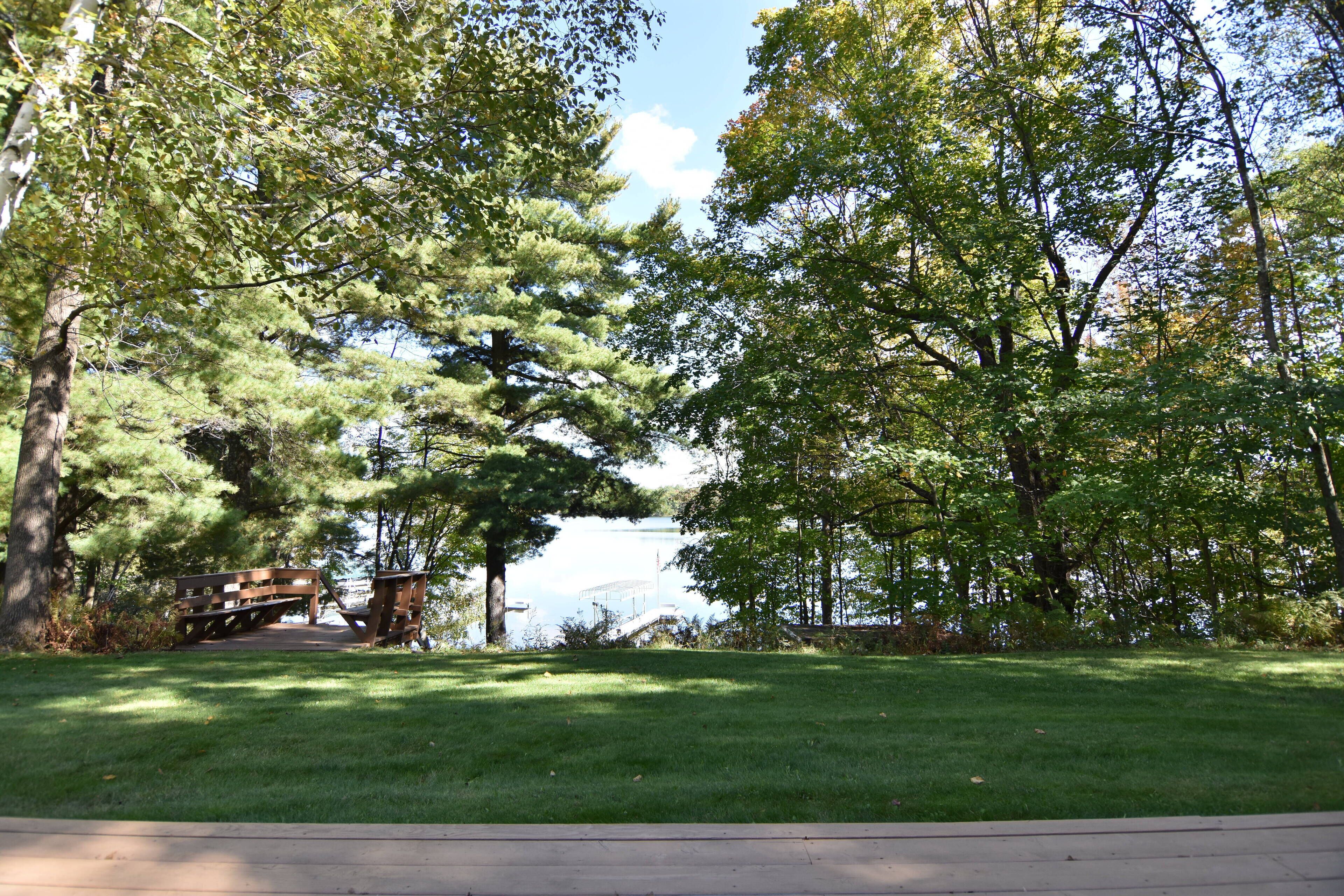 Un parque con una terraza de madera, una mesa de picnic y un lago al fondo.