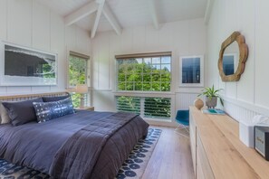 Una camera da letto con un letto grande, una scrivania con una radio e vista sul verde dalle finestre.