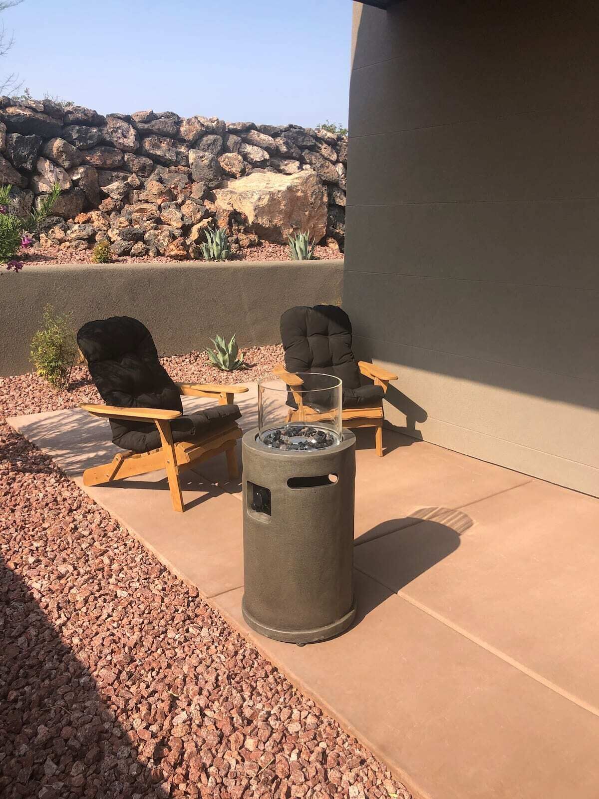 Un espace extérieur aménagé avec deux fauteuils noirs, une petite table et une poubelle cylindrique.