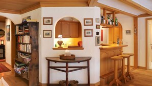 Una camera accogliente con una libreria in legno, un tavolino con un cesto e un angolo cottura con sgabelli e un bancone.