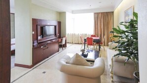 A modern hotel room with a flat-screen TV, a dining area with a red table and chairs, a sofa, and a large potted plant. - Wenzhou Lima Business Hotel (Binhai Industrial Park Branch, Wenzhou Longwan Airport) (Wenzhou)