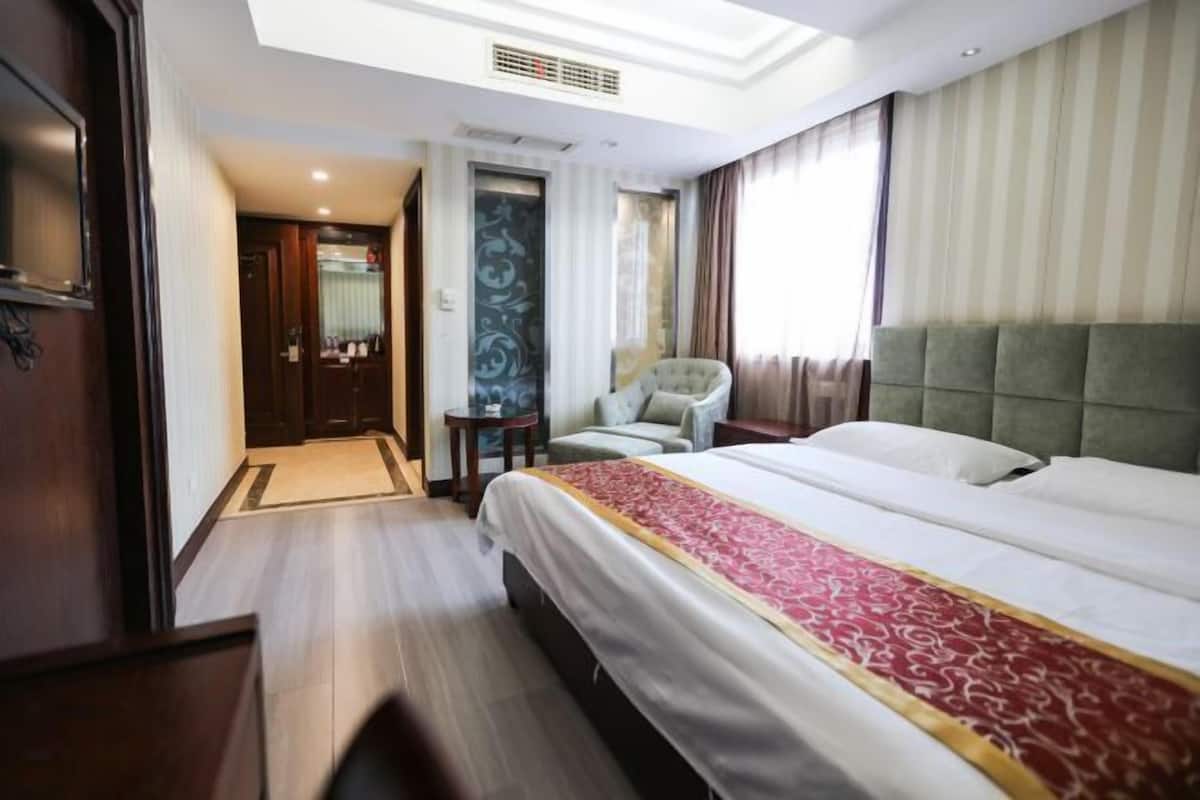 A hotel room with a large bed, a chair, a small table, and a door leading to another room.