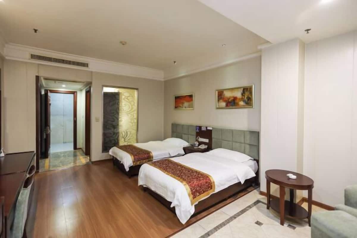 A hotel room with two beds, a desk, a chair, and artwork on the walls.