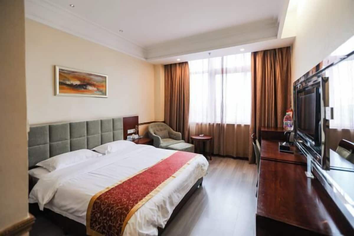 A hotel room with a large bed, a television, a chair, and a small table.