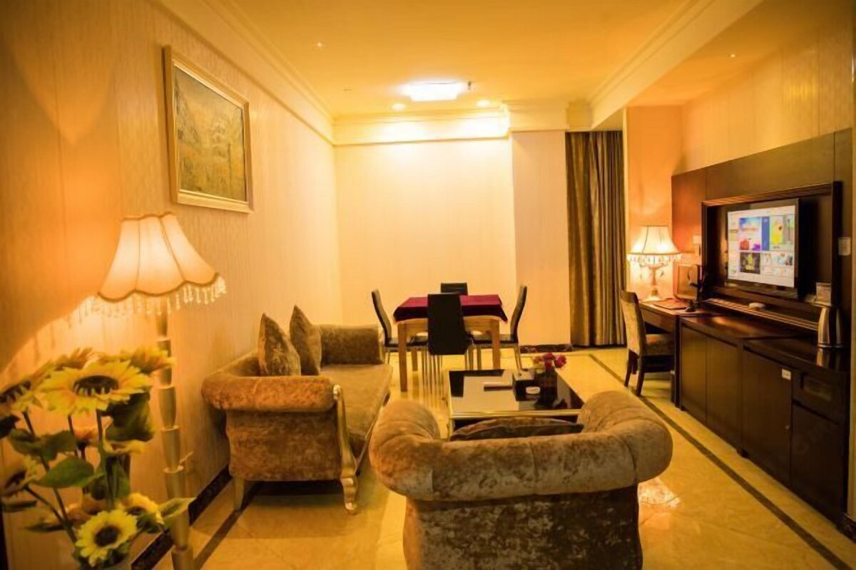 Una habitación de hotel con sofá, sillones, una mesa de comedor y televisión.