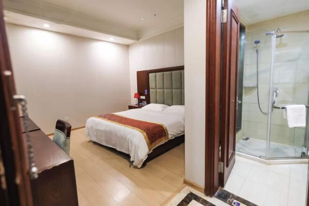 A hotel room with a bed, a desk, and a shower area.