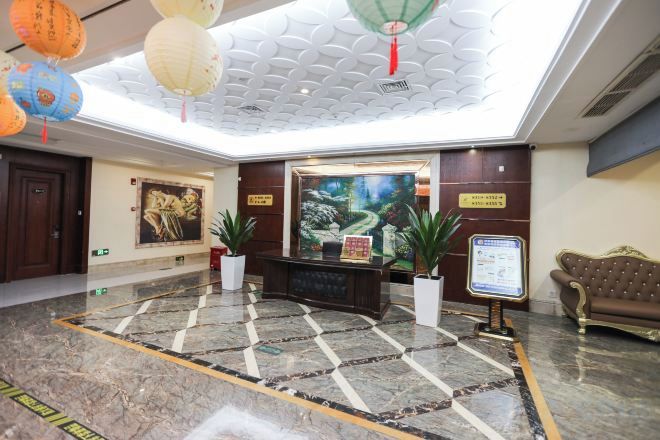 A hotel lobby with a reception desk, potted plants, a sofa, and a large painting on the wall.