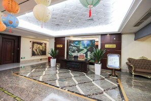 A hotel lobby with a reception desk, potted plants, a sofa, and a large painting on the wall. - Wenzhou Lima Business Hotel (Binhai Industrial Park Branch, Wenzhou Longwan Airport) (Wenzhou)