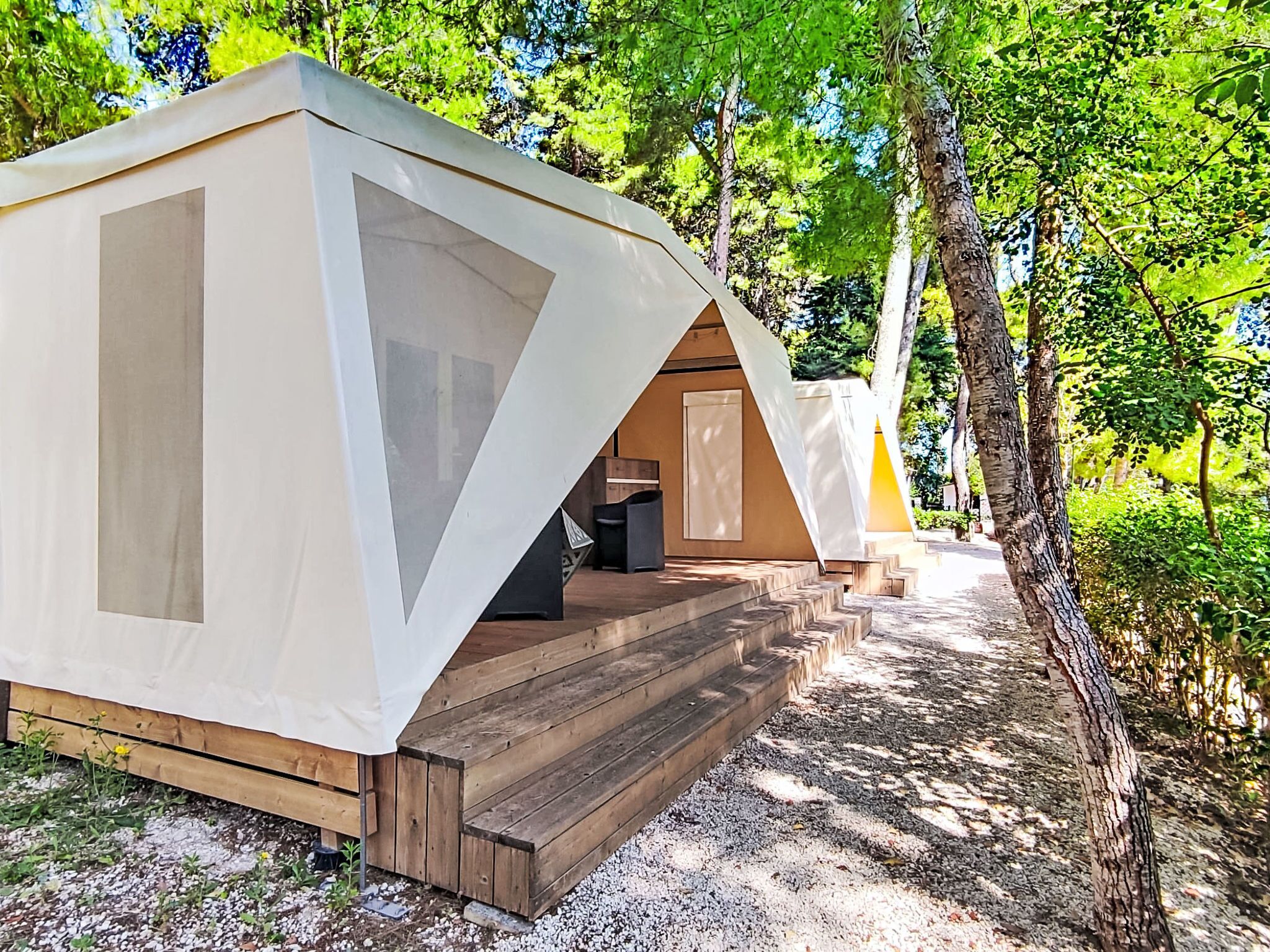 Una hilera de cabañas modernas con forma de tienda, terrazas de madera y un bosque de fondo.