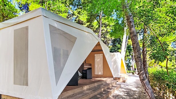 A row of modern, tent-like cabins with wooden decks and a forested backdrop.