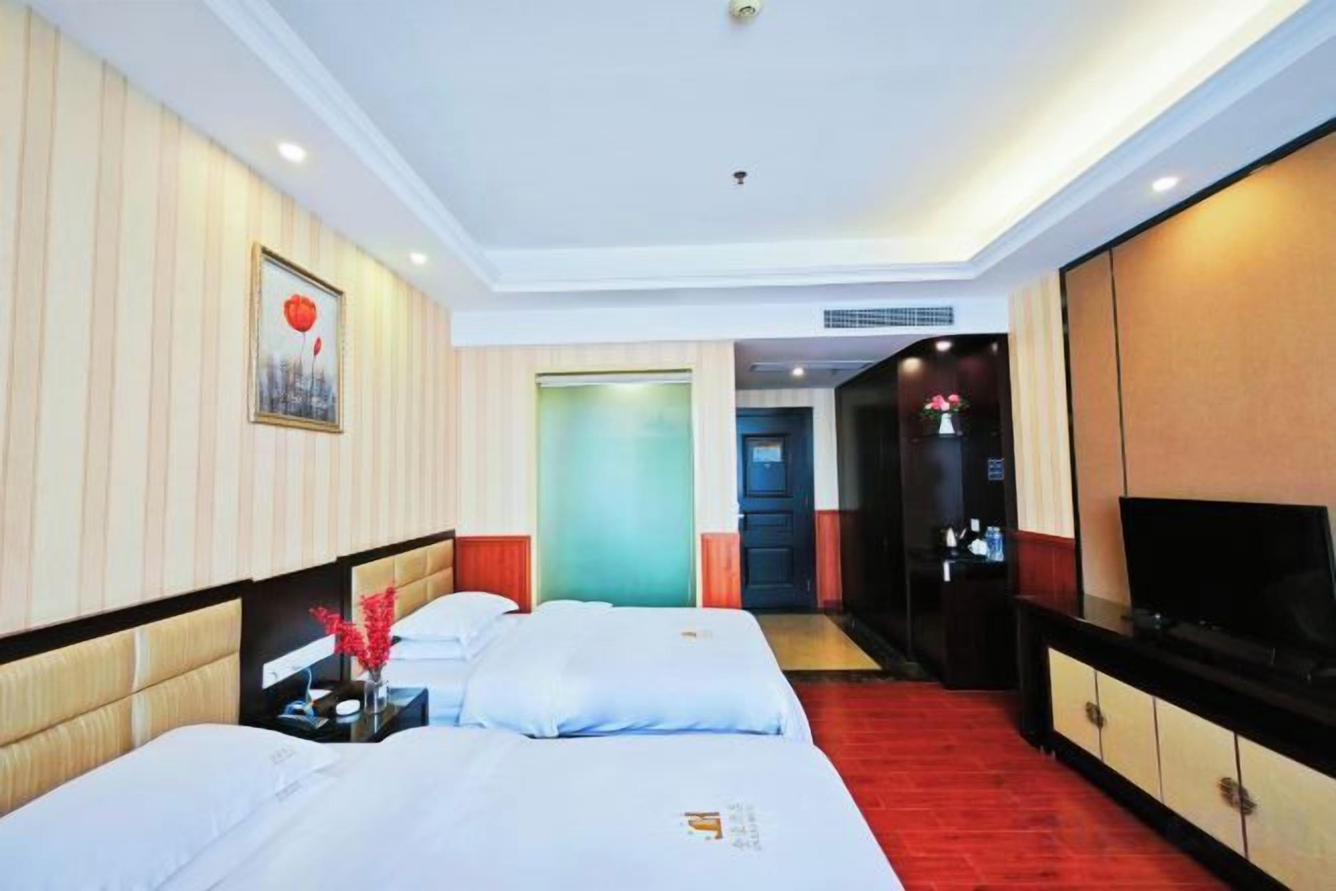 A hotel room with two beds, a TV, a desk, and a red carpet.