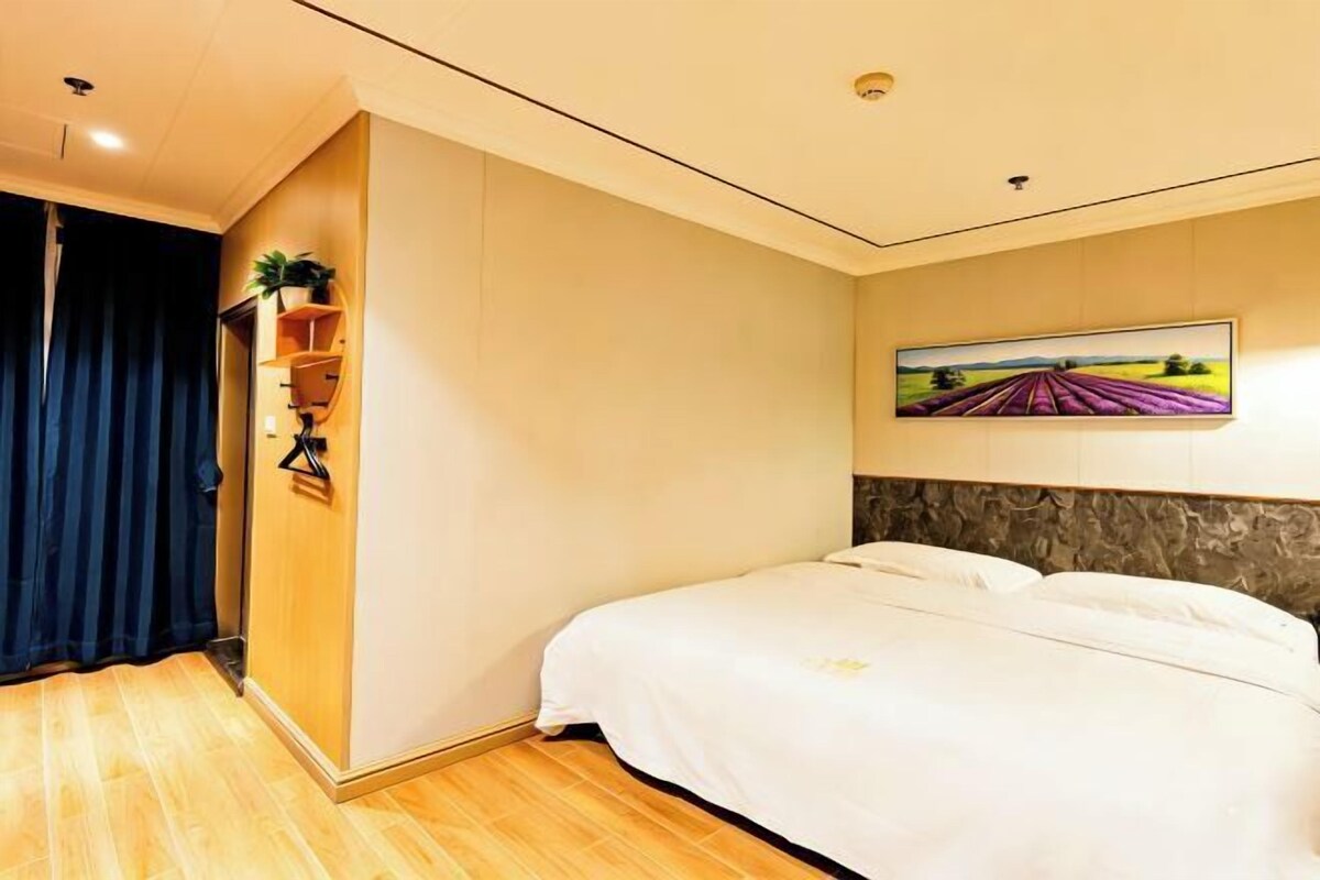 Quarto de hotel com uma cama, um quadro na parede, uma planta e uma estante de madeira.