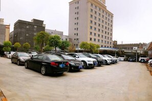 A parking lot with multiple cars, a building with a flat facade, and a few trees. - Jinhao Business Hotel (Lufeng)