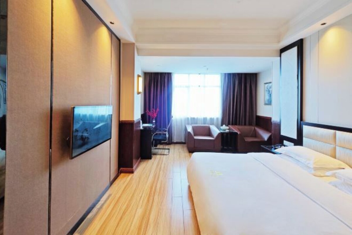 Quarto de hotel com uma cama grande, uma mesa, uma cadeira e uma televisão.