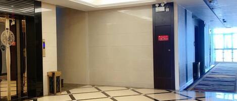A hotel lobby with a check-in desk, a reception area, and a staircase leading to another floor.