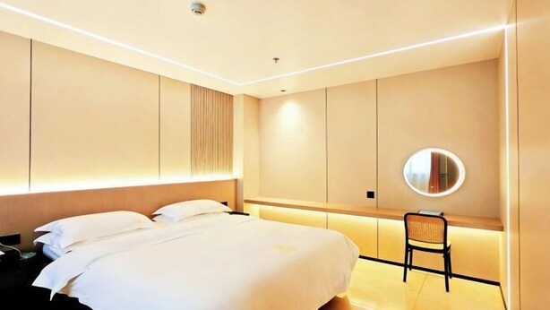 A modern hotel room with a large bed, a bedside table, a chair, and a round mirror on the wall. - Jinhao Business Hotel (Lufeng)